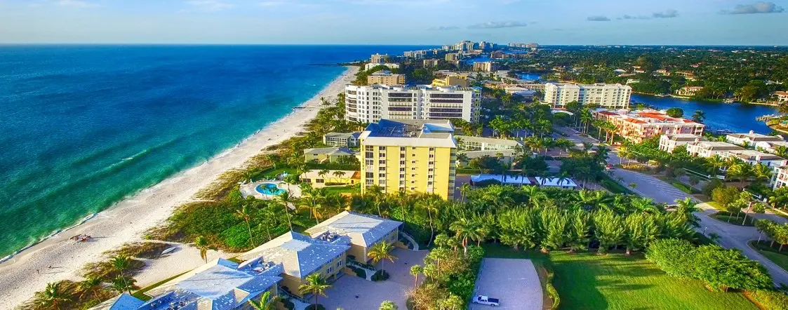 A view of the beach from above shows buildings, palm trees and ocean.