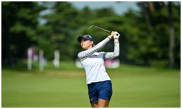 A woman swinging at the golf ball on a course.